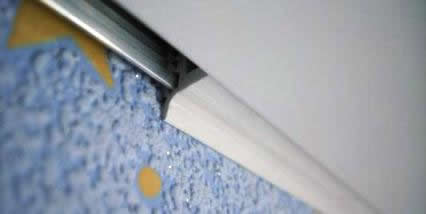 Установка плинтуса. Плинтусом для натяжного потолка может служить как щелевой фиксатор, так и специально предназначенная для этого планка. Закреплять последнюю нужно ПОД, а не НА потолок